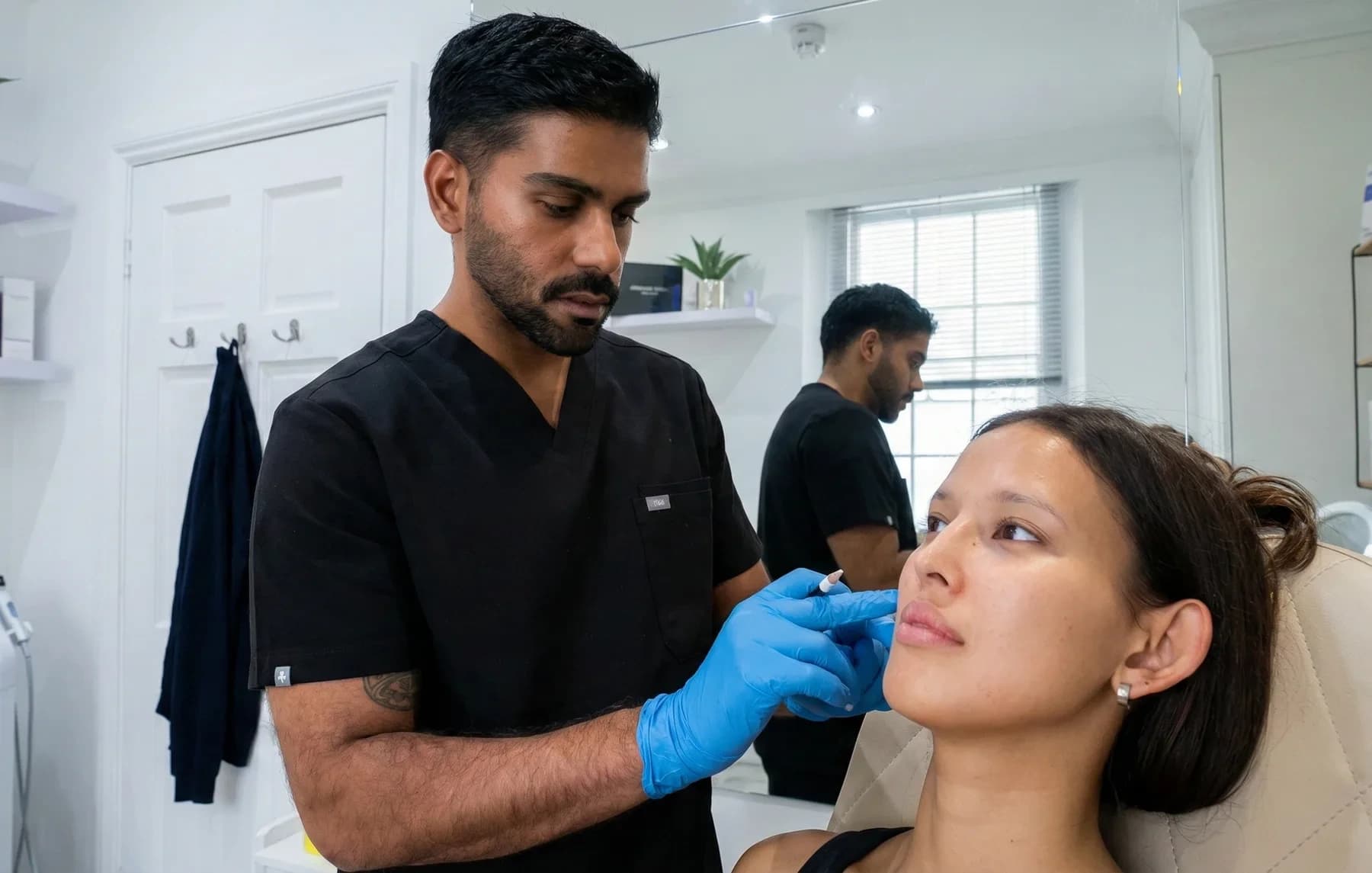 A clinician in black scrubs marking a seated patient's lower face with a white pencil before an injectable treatment at the London clinic